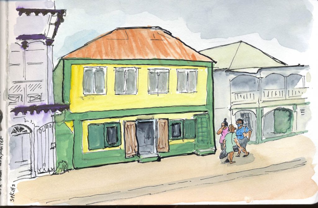 Ink and wash of a street in Basseterre, with a green and yellow building, a local cafe